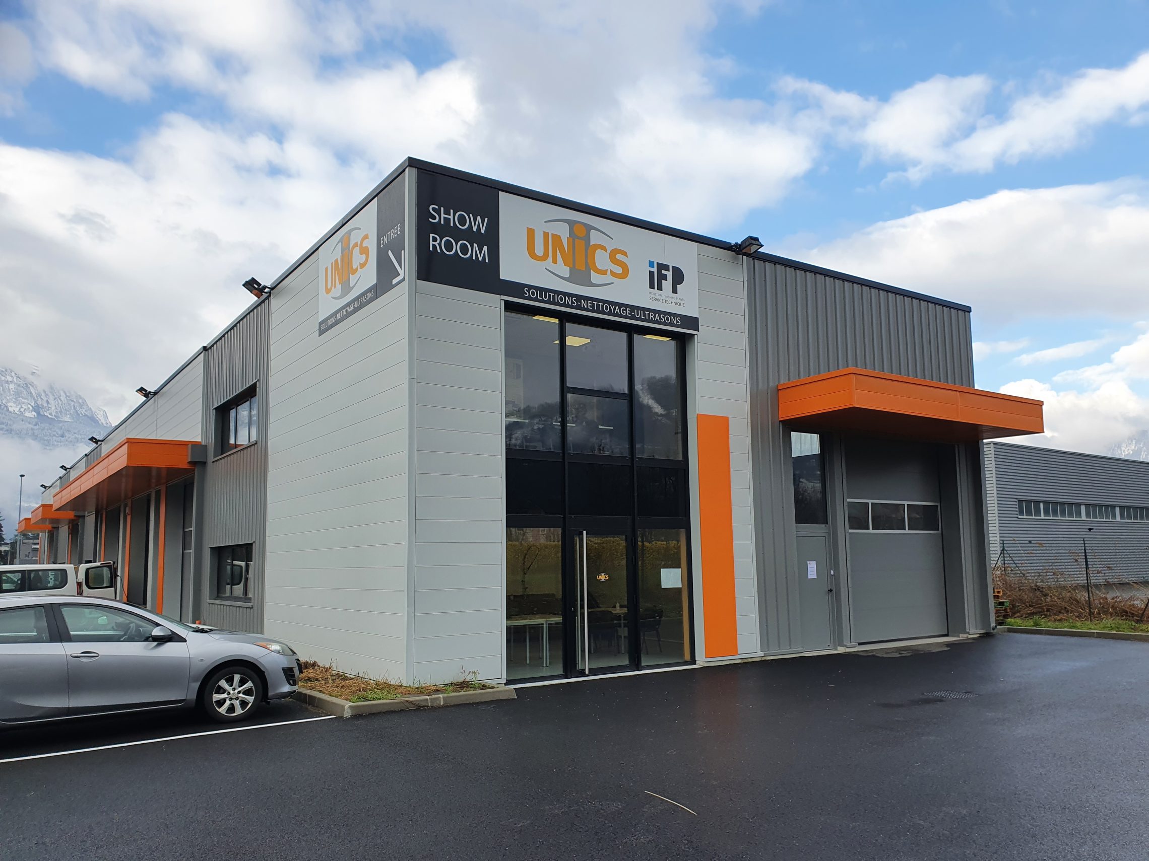 Bâtiment UNICS à Cluses : enseigne SHOW ROOM, logos UNICS et iFP en façade, montagnes de la vallée de l'Arve en arrière-plan